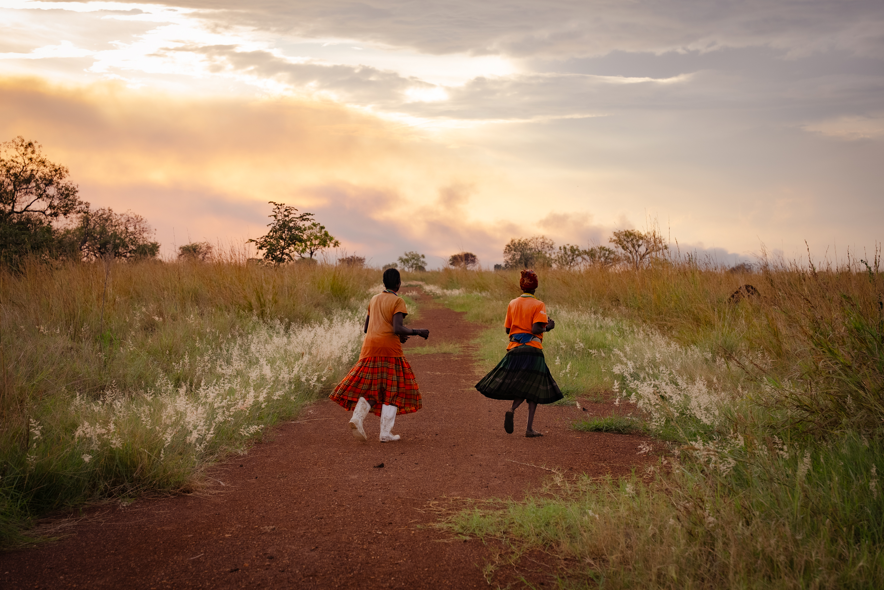 Two women walking a red-earth path at sunset