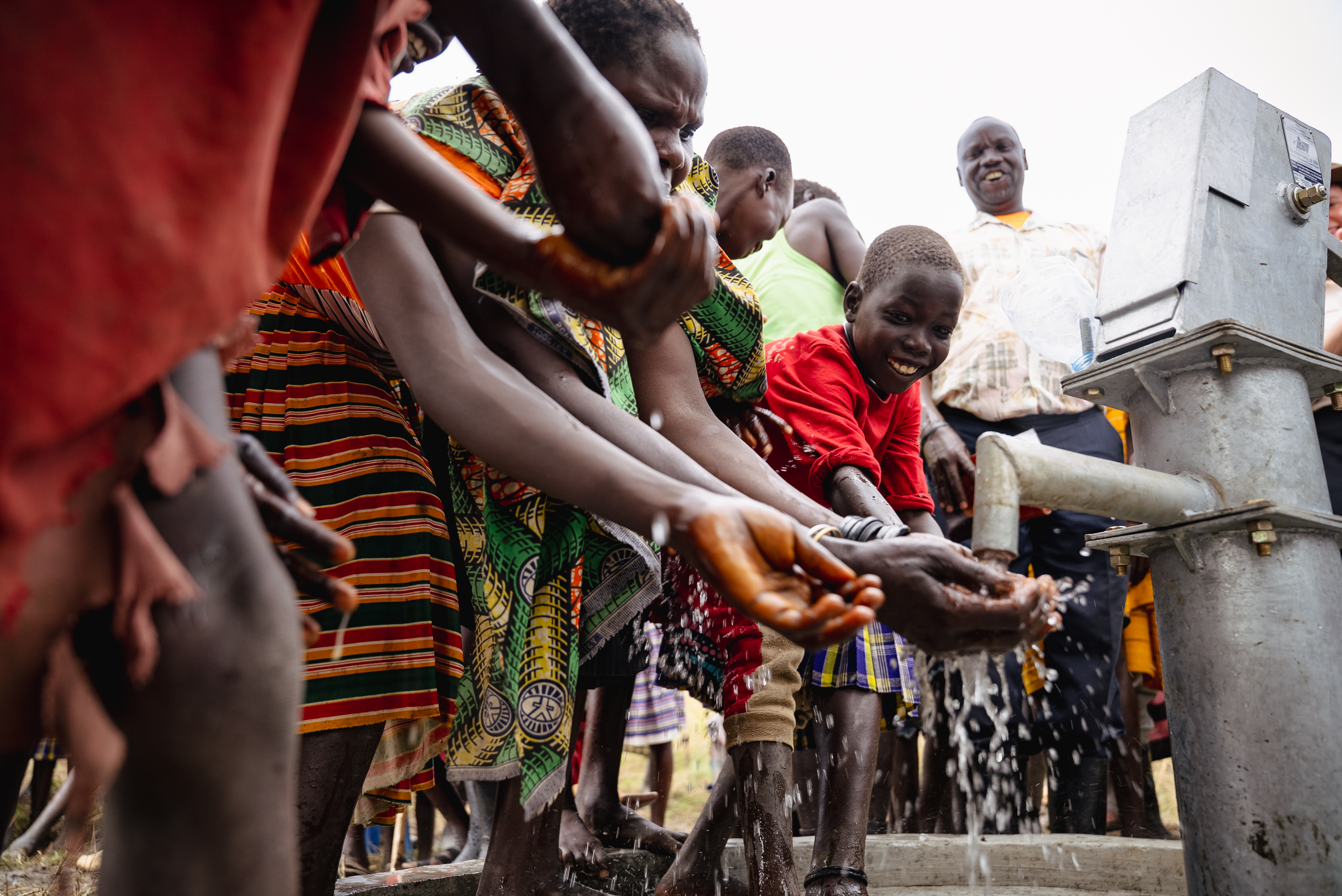 Hands cupped under the borehole spout as clean water runs