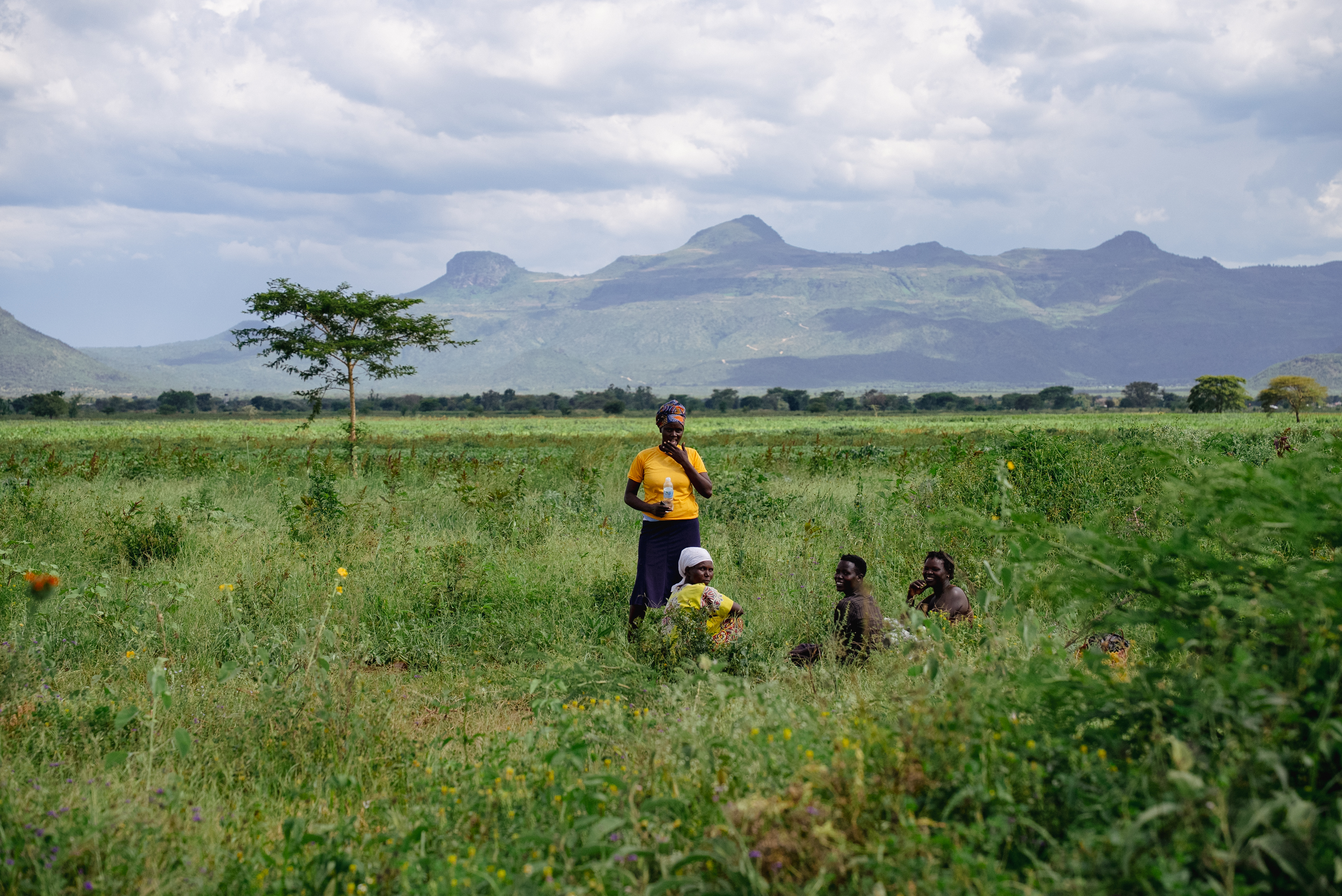 Women resting in a green field with the Karamoja hills behind